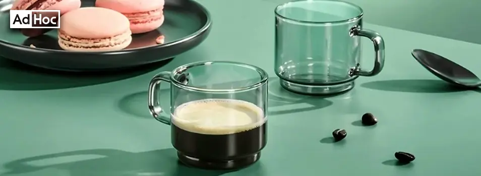 Tazas de vidrio apilables AdHoc con espresso junto a macarons y granos de café