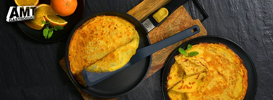 Sartenes AMT Gastroguss con crepas doradas, naranjas y menta sobre una tabla de madera